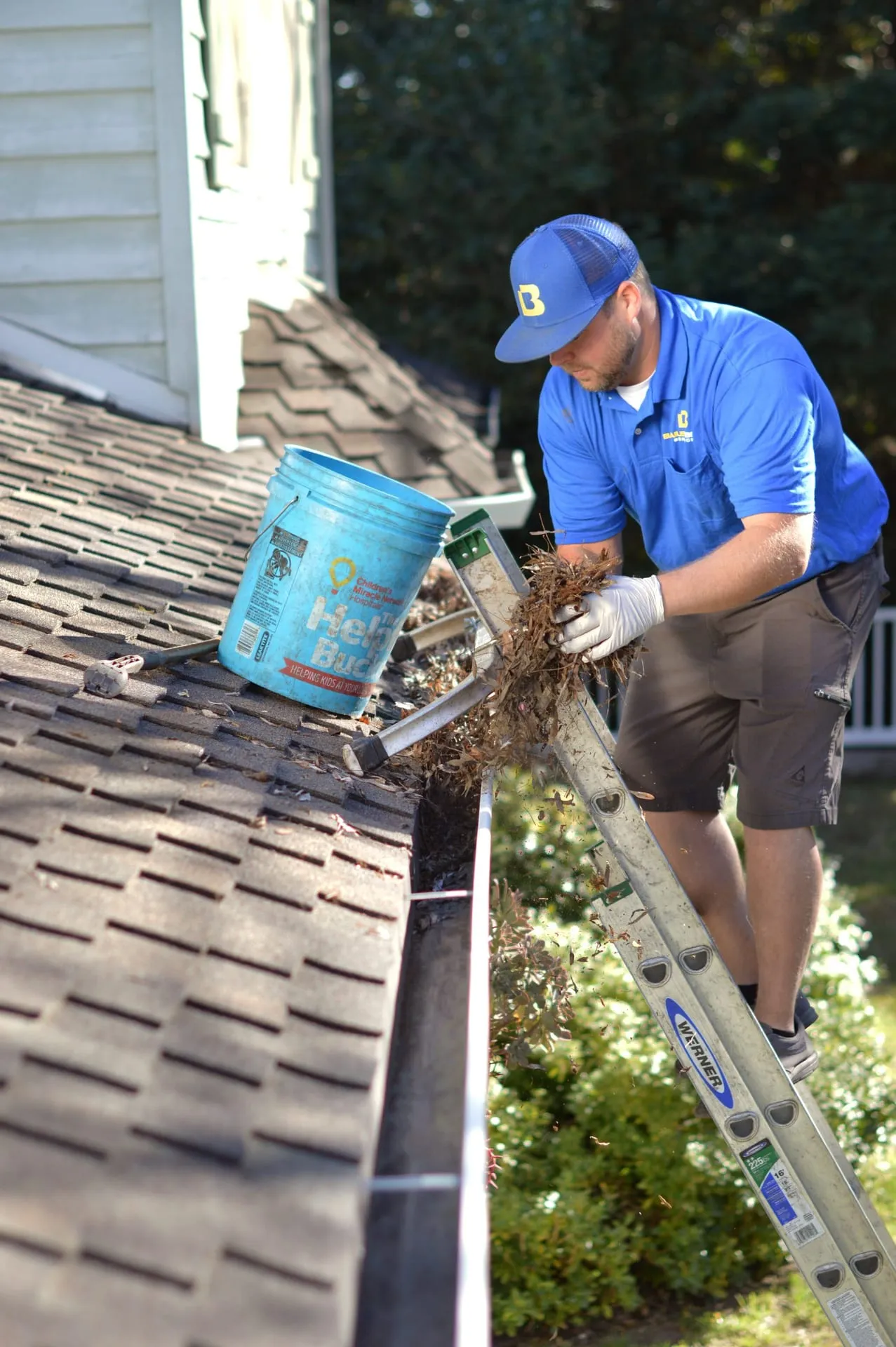 A Bailey Boys technician on a ladder clearing leaves and debris from the gutters of a Sacramento-area home