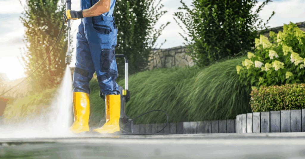a man doing house power washing.he is seen without the upper part of his body, only his yellow working boots and a hand holding a hose are shown