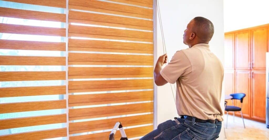a man checking his window blinds, looking to search online for "blind cleaning near me"