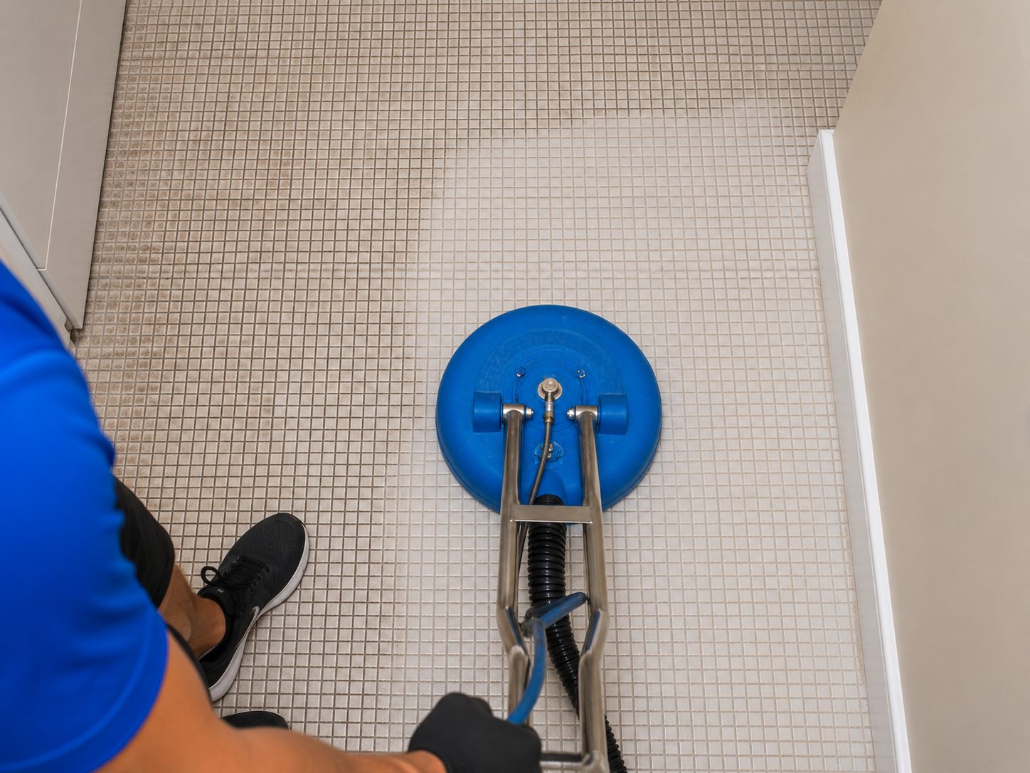 Overhead view of a rotary tool cleaning mosaic shower-floor tile and grout