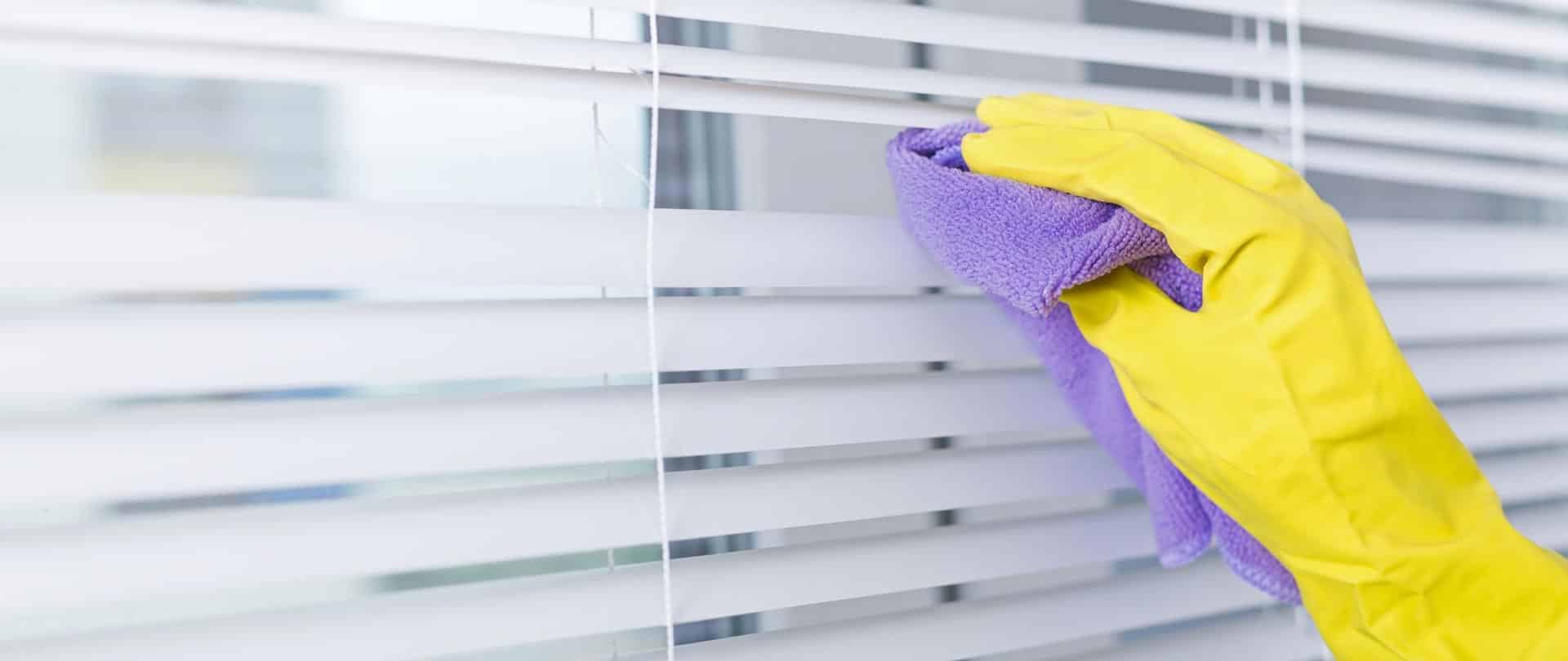 A gloved Bailey Boys technician cleaning white Venetian window blinds with a microfiber cloth in a Sacramento-area home